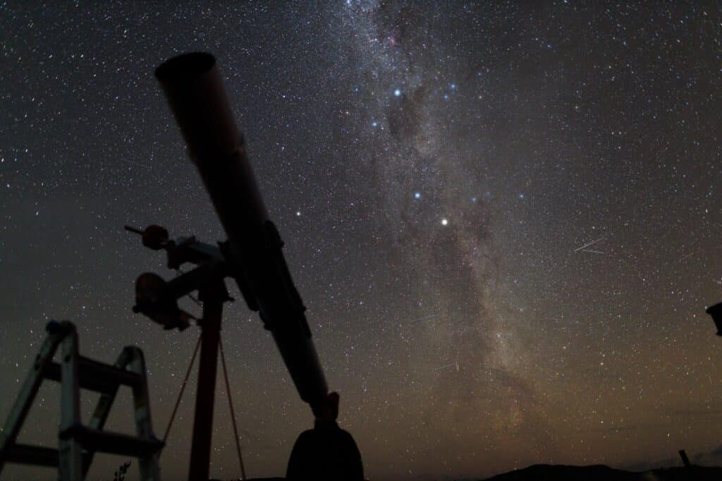 a person looking through an 8" refractor telescope while the centre of the Milky Way is rising in the background at the Wairarapa Dark Sky Reserve